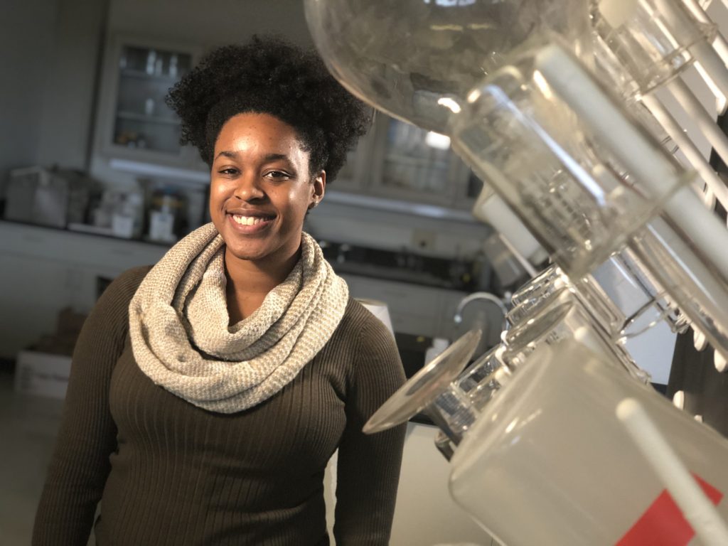 Simone stands in a research laboratory, with a lab bench behind her and glassware displayed to her left